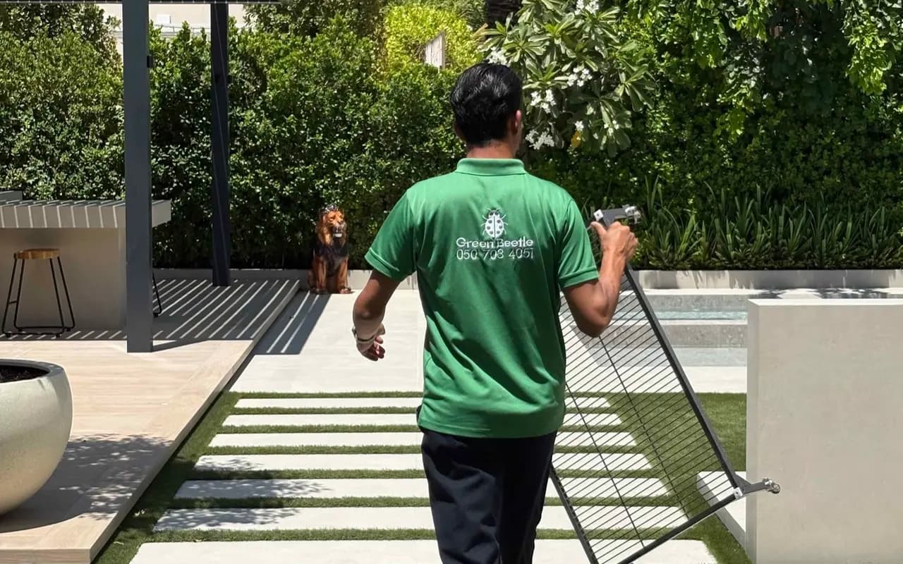 Green Beetle team member in a branded polo carrying equipment across a villa lawn