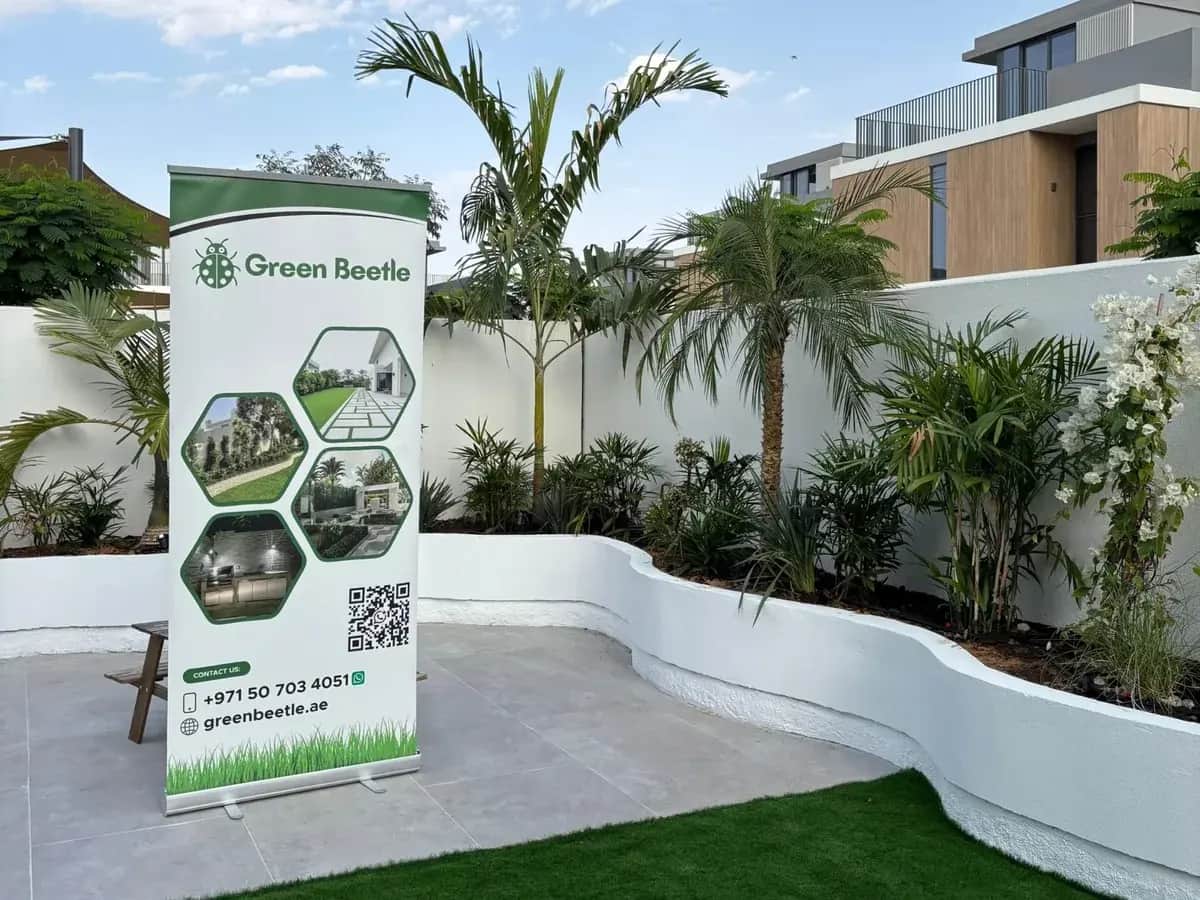 Curved white planters with palms around a lawn, with a Green Beetle banner