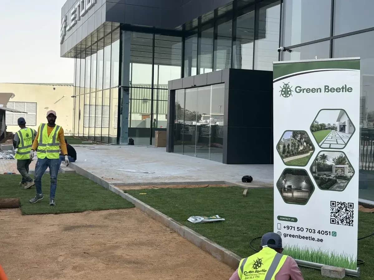 Green Beetle crew in hi-vis vests laying turf outside a showroom, with a Green Beetle banner